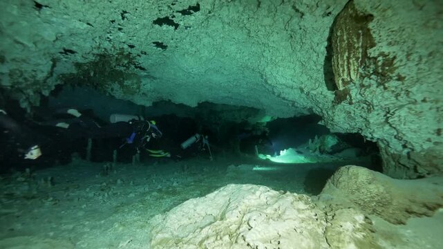 Diver moves across flat rocky bottom with cavern ceiling above in Cenote Dos Ojos, Quintana Roo, Mexico