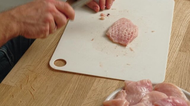 Person using meat tenderizer on raw chicken. Chef preparing pork loin slice with meat mallet on cutting board. Man tenderizing fillet. Cooking cutlets pounding poultry breast close-up. Culinary dish.