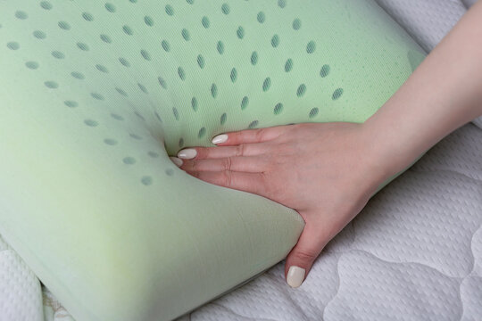 Close-up of a female hand pressing a perforated memory foam pillow. Demonstrates slow recovery, softness, and pressure relief of the material used for ergonomic support.
