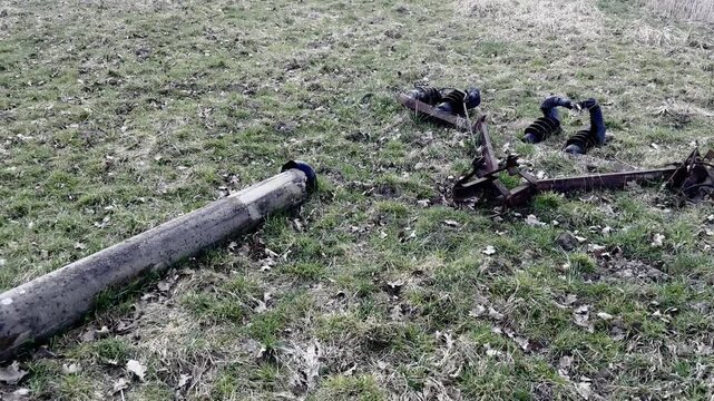 Fallen concrete utility pole and rusty electrical insulators lying in a field. Abandoned broken infrastructure and decay.