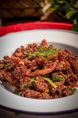 Fototapeta premium Traditional Northern Thai raw minced pork salad with blood and local spices, served with sticky rice in bamboo boxes and fresh vegetables on a wooden table. Local food preparation in Thailand.
