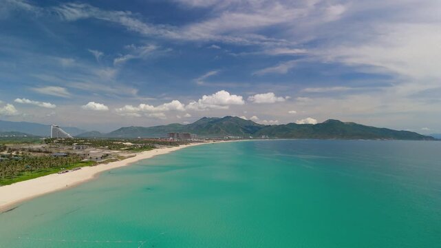 Experience a capturing the serene beauty of a Vietnam beach. White sand meets clear ocean waters with clouds gracefully moving above green mountains