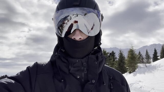 Close-up portrait of skier wearing helmet and reflective ski goggles showing reflection of snowy mountain slope. Active winter sports lifestyle