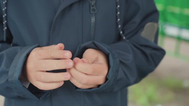 Closeup hands prepare backtoschool jacket, student fidgeting with button and zipper while waiting outdoors navy coat sleeves, shallow depth of field, subtle nervous energy and morning routine vibe