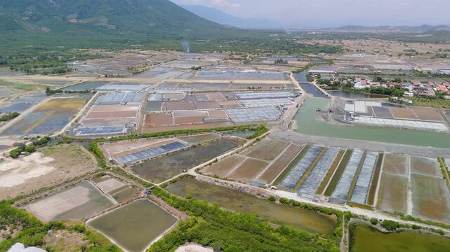 In Dok Let, Vietnam, there are salt fields near the beach. Machinery is visible working in the fields. The landscape shows water channels and fields under sunlight