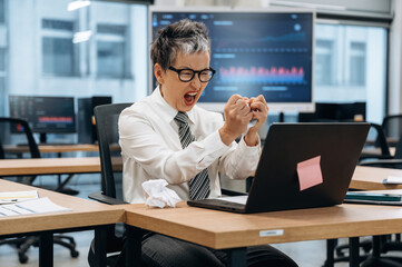 Obraz premium Business professional expressing frustration while working on a laptop in a modern office environment, showcasing the challenges of corporate life and stress management