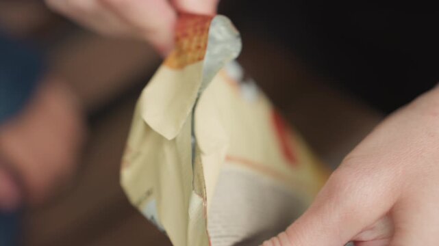 Student hands unwrapping ice cream cone, foil wrapper peeled back, waffle cone revealed, creamy scoop with chocolate chips, casual afterschool snack preparation, closeup of fingers and packaging