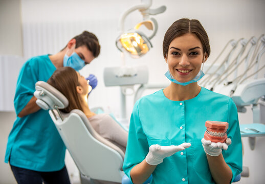 Dental assistant showing braces model in clinic.