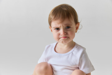 Naklejka premium Toddler girl sitting and making sad face with emotional expression isolated on white background. Concept of child emotions, mood changes, early psychology and communication of feelings.