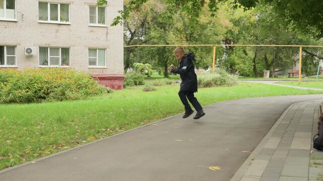 Child rushing happily. Child with excited face moves quickly through park toward educational building. Young boy with big smile dashes through autumn scenery carrying his school materials and bag