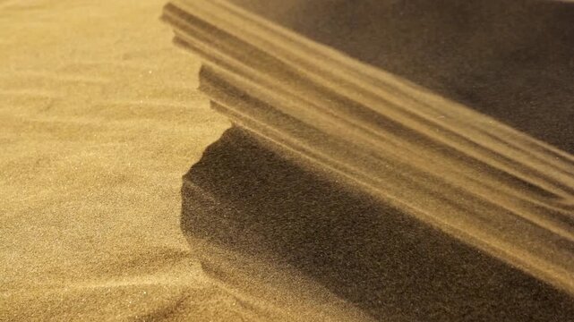 Strong wind sweeps a sand storm over the edge of a desert dune. Moving sand particles create dynamic surface patterns. Extreme close up detail shot