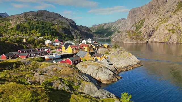 Traditional red and yellow cabins stand in the Nusfjord fishing village of the Lofoten Islands, Norway. Drone aerial reveals steep mountains surrounding the fjord of Nusfjord, Norway