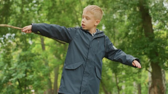Boy practices pretend sword combat. Child with focused look holding stick during imaginative adventure. Boy carefully practicing pretend sword fighting with stick before returning to school