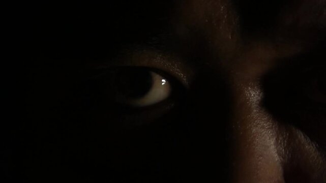 Extreme close up of a male face in deep shadows illuminated by warm light, the eyes darting around intensely.