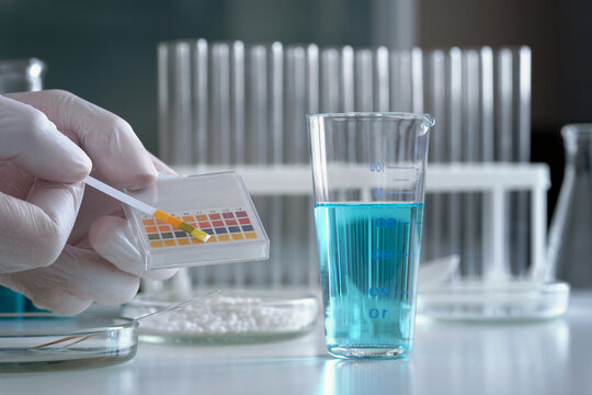 A scientist in a chemical laboratory takes measurements of the acid-base balance of a liquid in a glass flask.