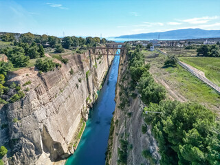 Fototapeta premium Aerial drone shot of Corinth Canal extending to distant sea horizon with surrounding landscape and blue sky, Greece