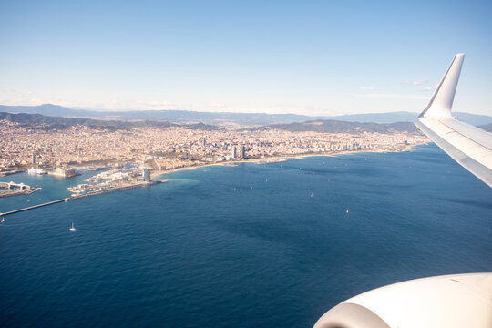 Clean commercial airplane wing flight travel aerial above coastline sea city showing transport in Barcelona Spain modern aviation window view