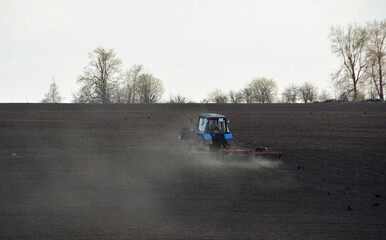 Fototapeta premium Tractor working in a dusty field, preparing soil for planting