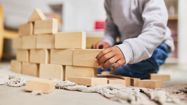 Child building wooden block wall structure at home floor close up hands. Concept of early engineering skills, fine motor development and creative construction play activity.