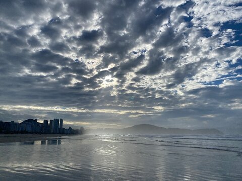 nuvens  e c&eacute;u azul em um amanhecer na praia com alguns pr&eacute;dios na orla refletindo em espelho d&aacute;gua  na cidade de Praia Grande