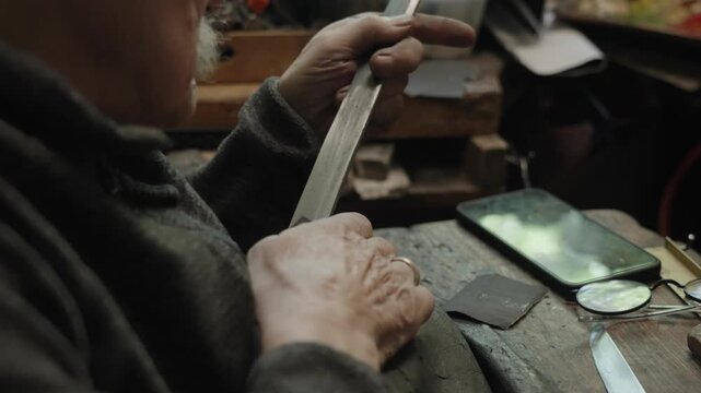 Elderly craftsman working in his old workshop, carefully restoring collectible Japanese bladed weapons