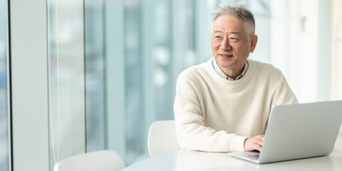 Fototapeta premium Elderly man smiling while using laptop in office workspace