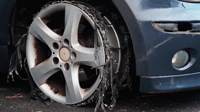 Front wheel of blue car with completely destroyed and shredded tire after burnout or accident.