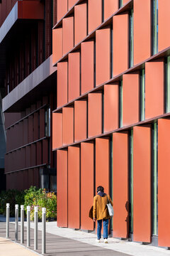 Lone pedestrian framed by modern urban architecture on a textured facade with repeating pattern and long shadows showing strong color in paris france