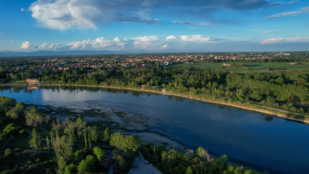 Po River marking the Emilia Romagna and Lombardy border with Cremona's skyline and Torrazzo tower rising above green floodplain fields under a summer sky