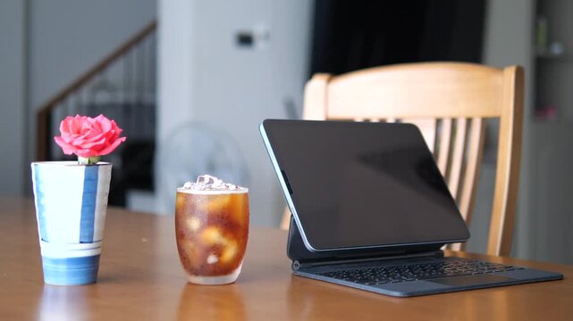 Close-up of refreshing iced Americano coffee with condensation on glass next to tablet and pink rose for lifestyle and break time concept
