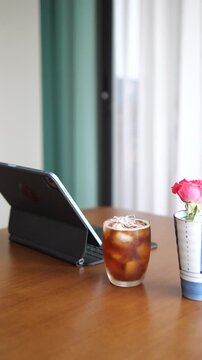 Close-up of refreshing iced Americano coffee with condensation on glass next to tablet and pink rose for lifestyle and break time concept