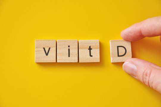 Hand placing vitamin D letter block, minimal healthcare and supplementation concept