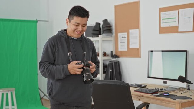 Man in hoodie adjusting camera with hands and checking lens in studio green screen workspace; content creativity.