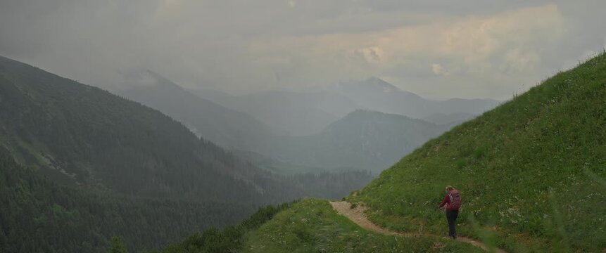 Distant hiker on mountain path overlooking vast forested valley