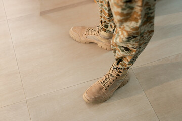 Obraz premium Close up of soldier boots and camouflage uniform standing on floor, representing military lifestyle, discipline, readiness, strength, and professional army equipment concept.