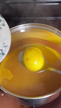 Boiled eggs colored with turmeric are taken out with a spoon and placed in a bowl, with steam rising from the pot.