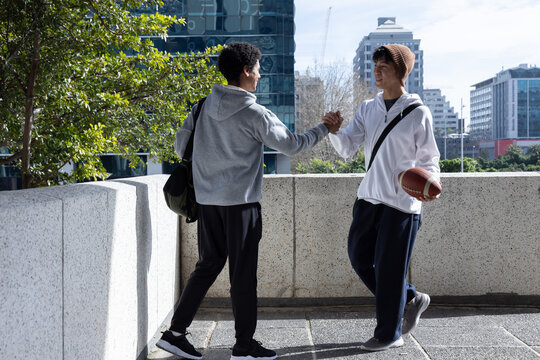 Clasping hands, holding football, diverse teenage males standing on rooftop with bags in sportswear