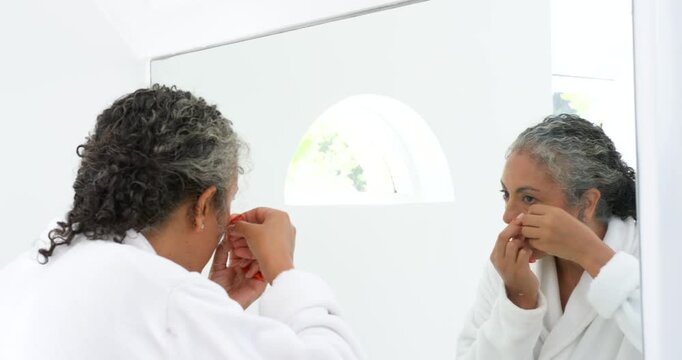 Senior African American woman holding red patch, applying patch for skin in robe at bathroom mirror