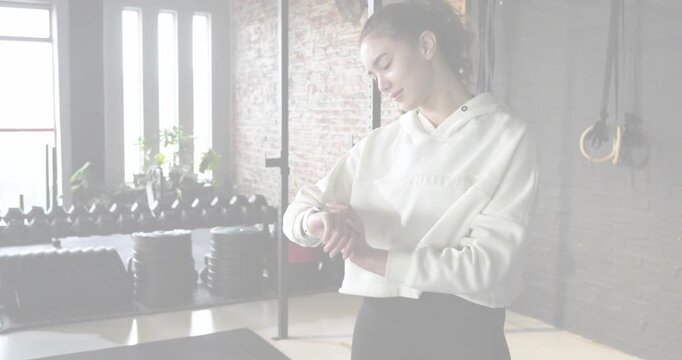 Woman adjusting smartwatch in gym while scanlines clearing, dumbbells visible, preparing workout
