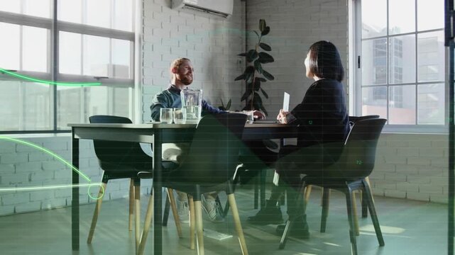 Vertical video: Discussing pair in workwear as woman showing tablet at table green graphics forming