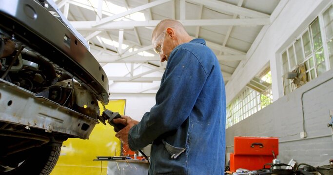 Grinding mechanic in blue coverall sanding car frame at workshop with grinder, toolbox, copy space