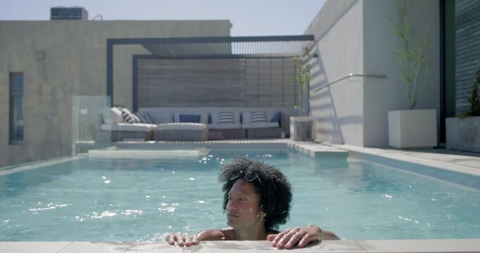 African American man feeling midday sun, swimming to rooftop pool edge, gripping coping, smiling