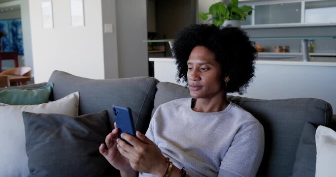 Adult man holding blue smartphone, tapping and scrolling while reading messages on gray couch