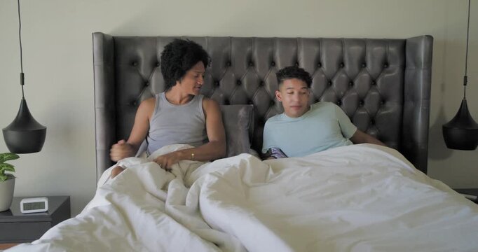 Diverse male partners after talking by tufted headboard, standing and making bed with white duvet