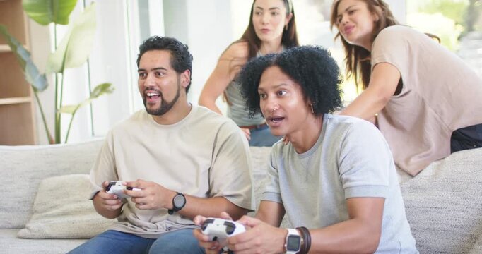 Diverse friends in living room, two male players holding white controllers reacting to game events