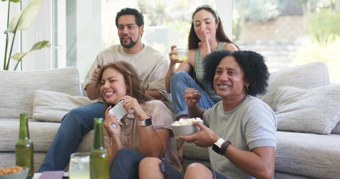 Diverse friends sitting on sectional couch holding controllers and popcorn, celebrating game win