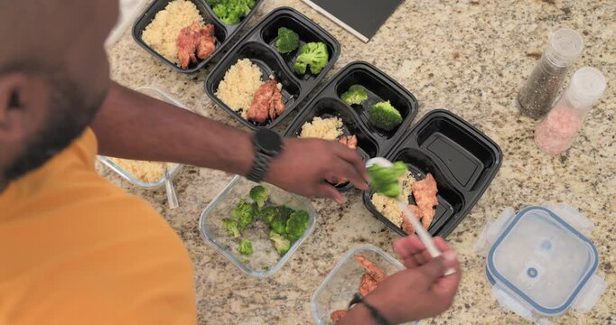 With trays Mid Adult man scooping broccoli into black trays on kitchen counter for meal prep