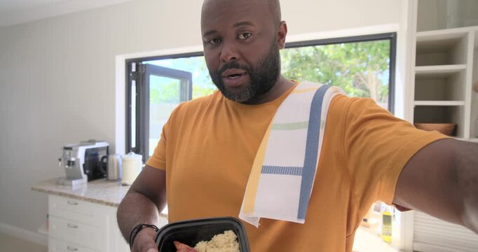 Man presenting and tilting meal container to camera after cooking in home kitchen, striped towel
