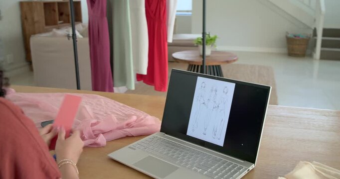 Woman viewing laptop renderings, picking up pink fabric and comparing trim for color match