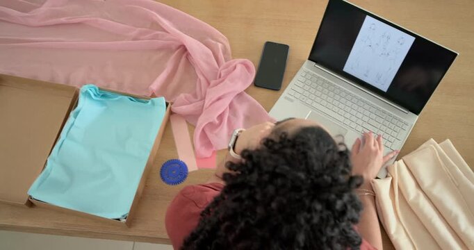 Woman sitting at worktable noticing pink fabric and opening laptop, comparing sketches and packing